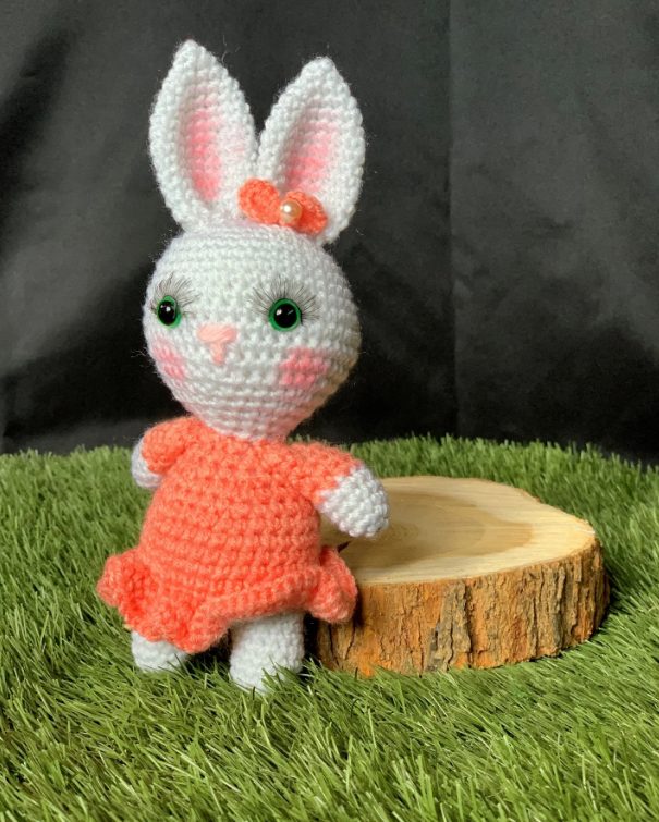 Lapine blanche au crochet avec robe corail sur herbe